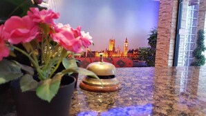 A hotel lobby with a reception desk, a potted plant, and a backdrop of a cityscape. - Barking Hotel  (Barking)