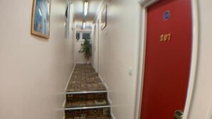 A hallway with a patterned carpet, a red door with the number 207, and a framed picture on the wall. - Barking Hotel  (Barking)