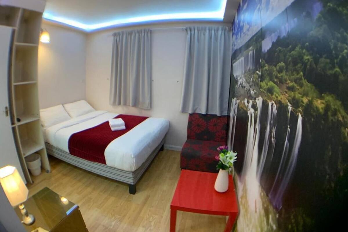 Ein Hotelzimmer mit einem Bett, einem kleinen Tisch mit einer Vase, einem an der Wand befestigten Regal und einem großen Poster.
