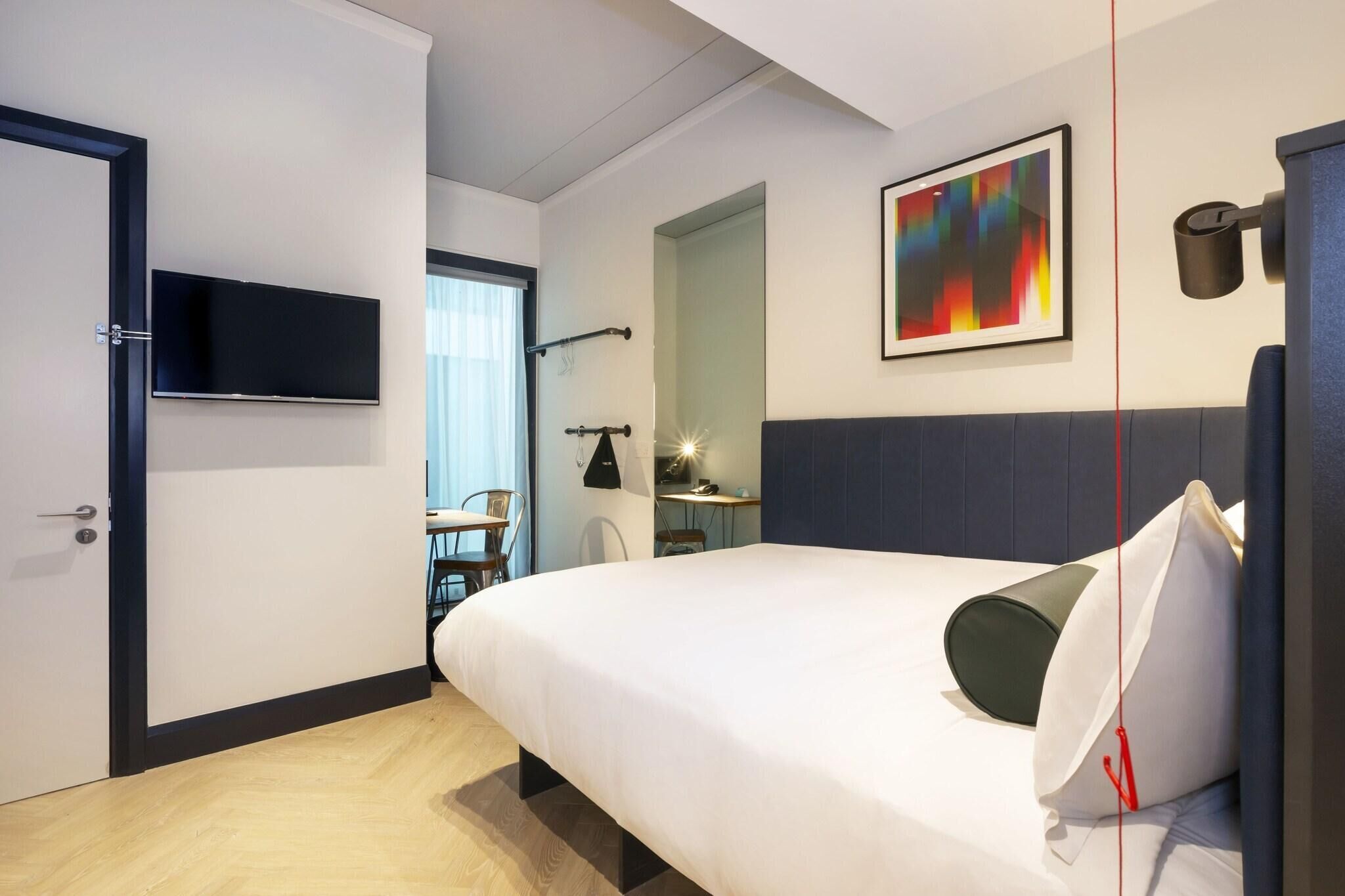 A hotel room with a bed, a TV, a desk, and a chair.