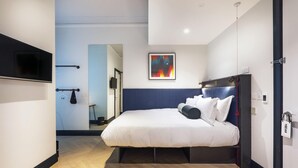 A modern hotel room with a bed, a flat-screen TV, a framed abstract painting, and a wooden floor. - Hendrick Smithfield (Dublin)