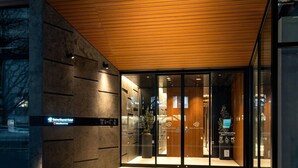 Una entrada de hotel moderna con fachada de vidrio, un alero de madera y un letrero que dice 'Our Citizenship'.