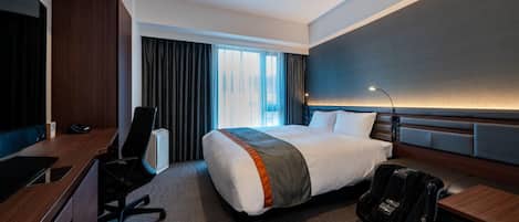 Habitación de hotel con cama, escritorio, silla y un ventanal con cortinas.