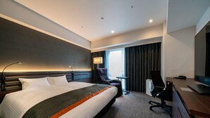 Quarto de hotel com uma cama grande, uma escrivaninha, uma cadeira, um abajur e uma televisão.