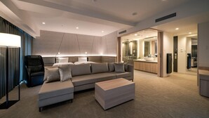 Una habitación de hotel moderna con un sofá grande, una mesa de centro y una zona de estar separada con una silla.