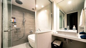 Uma casa de banho moderna com cabine de duche em vidro, banheira, espelho grande e toucador com artigos de higiene pessoal.