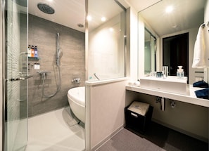 Un baño moderno con cabina de ducha de vidrio, bañera, espejo grande y tocador con artículos de aseo.