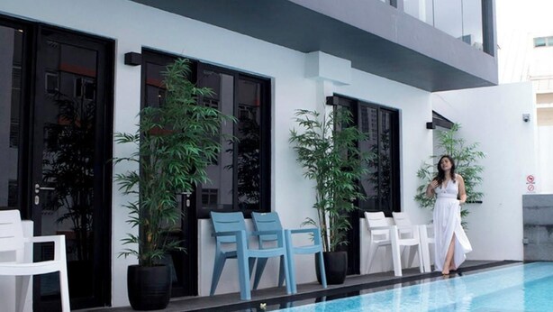 Un espace aménagé au bord de la piscine, avec un bâtiment moderne, des sièges d’extérieur et des plantes en pot.