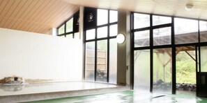 Un espacio interior amplio con ventanas grandes, techo de madera y piso verde.