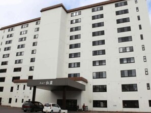 Un edificio de varios pisos con fachada plana, múltiples ventanas y un área de acceso cubierta.