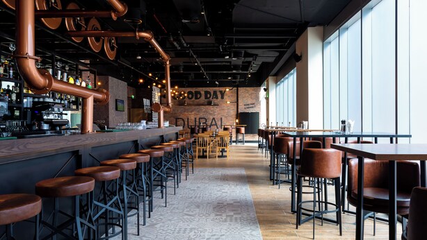 A bar area with stools, a counter, and a patterned floor. - Premier Inn Dragon Mart Hotel (Dubai)