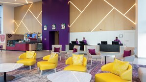 A modern lobby with yellow sofas, a reception desk, and a large TV screen. - Premier Inn Dragon Mart Hotel (Dubai)