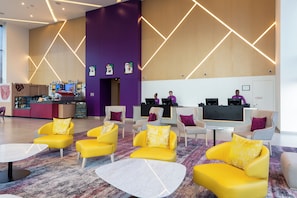 Eine moderne Lobby mit gelben Sofas, einem Empfangsbereich und einem großen Fernsehbildschirm.