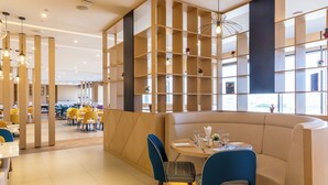 A modern dining area with a booth seating arrangement, a central table with a vase of flowers, and a decorative wall with shelves. - Premier Inn Dragon Mart Hotel (Dubai)