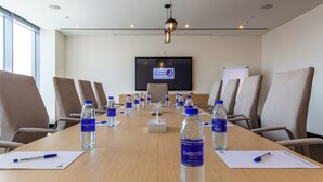 A conference room with a long table, chairs, water bottles, pens, and a television screen. - Premier Inn Dragon Mart Hotel (Dubai)