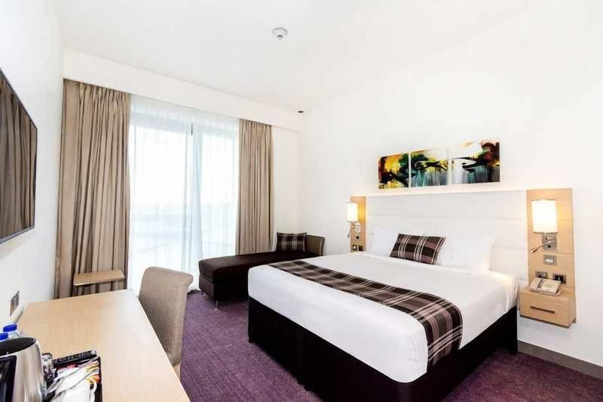 A hotel room with a large bed, a desk, a chair, and a TV.