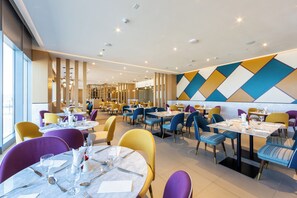 A modern dining area with round tables, chairs, and a geometric wall design. - Premier Inn Dragon Mart Hotel (Dubai)