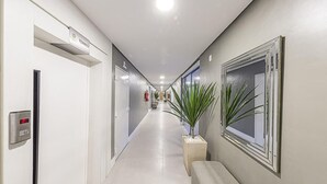 Corredor de hotel com um banco, um extintor de incêndio e uma placa indicando o caminho para o restaurante.