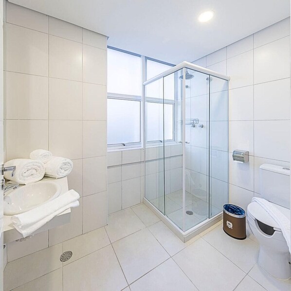 A modern bathroom with a glass-enclosed shower, a sink with a mirror, and a toilet. - Hotel Global (São Paulo)