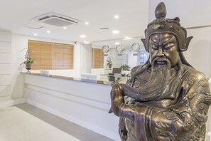 A reception area with a statue, a reception desk, and a window with blinds. - Hotel Global (São Paulo)