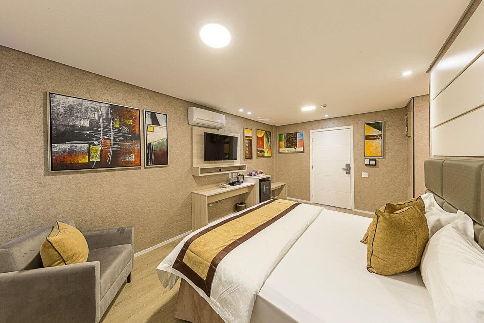 A hotel room with a bed, a desk, a chair, a TV, and artwork on the walls.