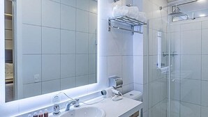 A modern bathroom with a large mirror, two sinks, a toilet, and a glass-enclosed shower. - Hotel Global (São Paulo)