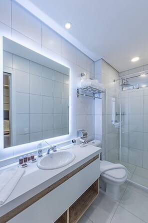 A modern bathroom with a large mirror, two sinks, a toilet, and a glass-enclosed shower.