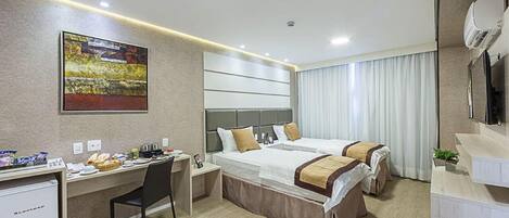 A hotel room with two beds, a desk, a chair, a dining table, and a large window with curtains.