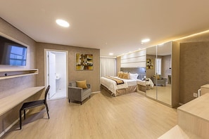A modern hotel room with a bed, a desk, a chair, a large mirror, and artwork on the walls.