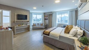 Quarto de hotel com cama, televisão, secretária e vista para a cidade.