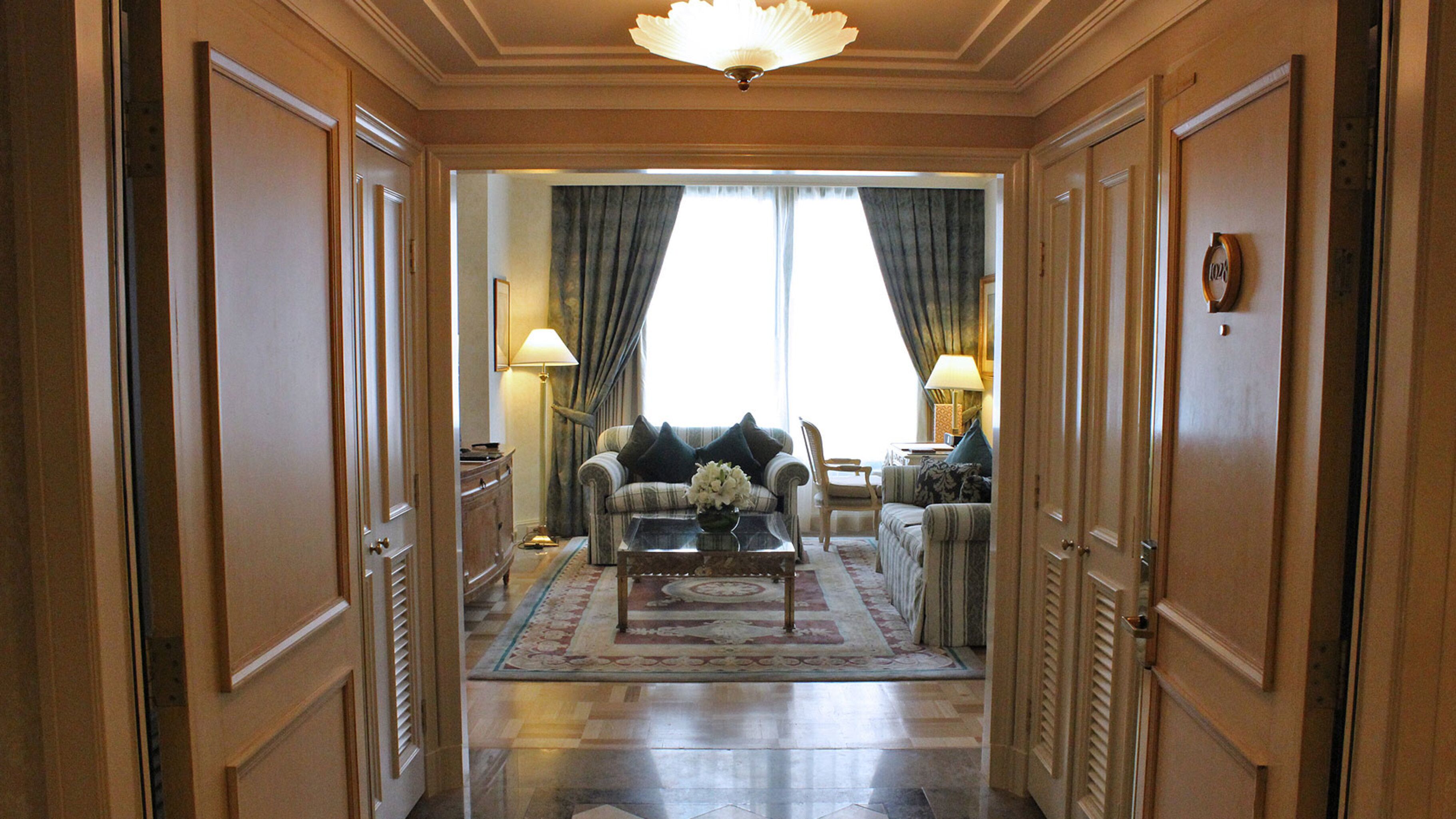 A hallway leading to a living room with a sofa, armchairs, a coffee table, and a chandelier.