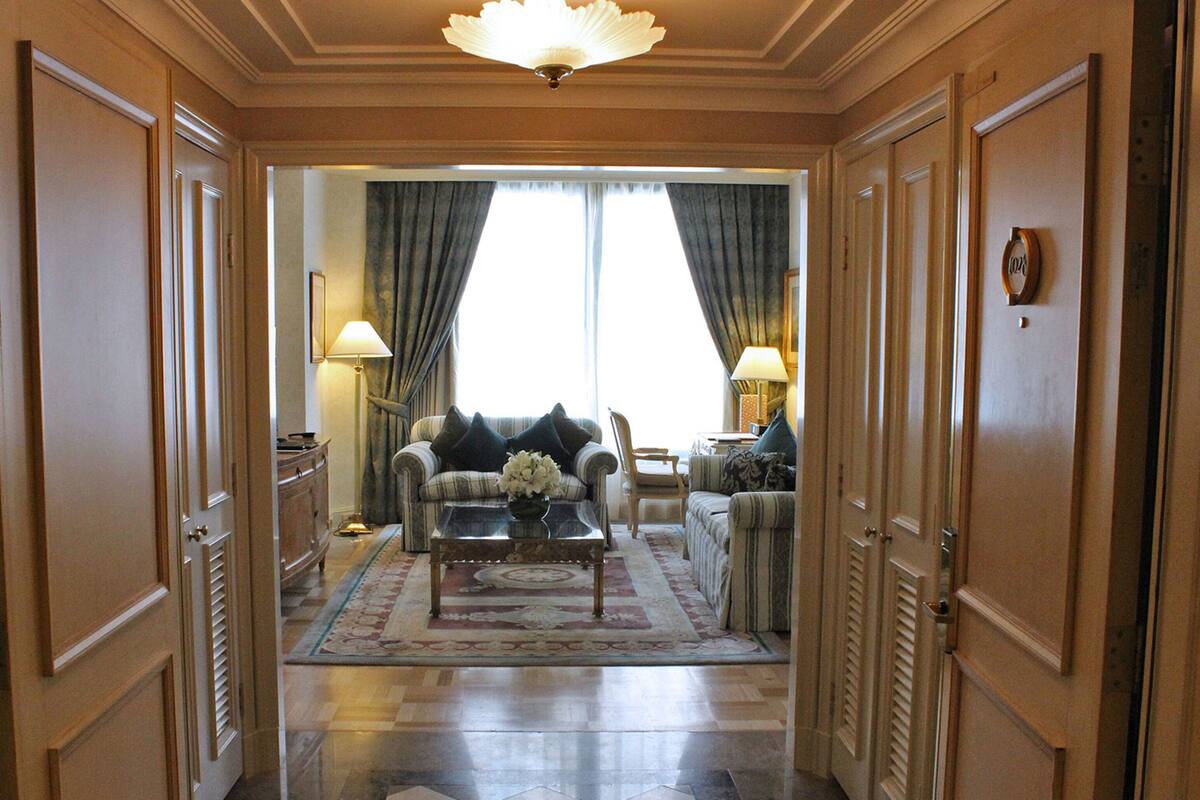 A hallway leading to a living room with a sofa, armchairs, a coffee table, and a chandelier.