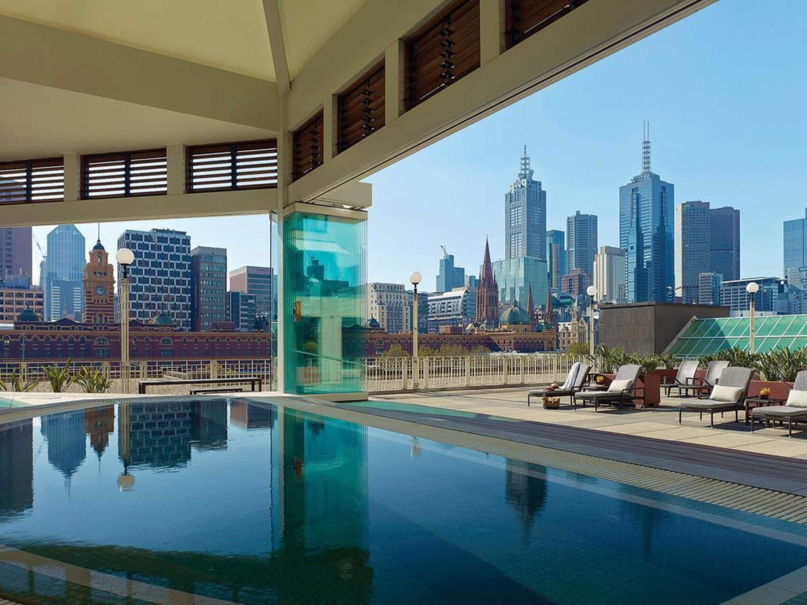 Une piscine sur le toit offrant une vue panoramique sur la ville, des chaises longues et une structure entièrement vitrée.