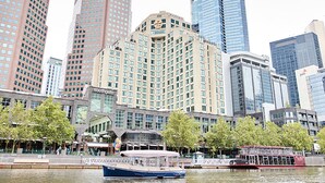 A waterfront hotel with a large building, a boat docked in the water, and a red double-decker bus in the background. - The Langham Hotel, Melbourne (Melbourne)