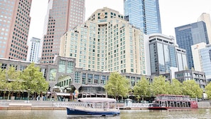 Ein Hotel am Wasser mit einem großen Gebäude, einem Boot, das im Wasser liegt, und einem roten Doppeldeckerbus im Hintergrund.