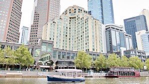 A waterfront hotel with a large building, a boat docked in the water, and a red double-decker bus in the background. - The Langham Hotel, Melbourne (Melbourne)