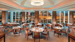 A spacious dining area with multiple tables and chairs, large windows offering a city view, and a central chandelier. - The Langham Hotel, Melbourne (Melbourne)