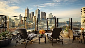 A terrace with wicker chairs, a table, and potted plants, overlooking a cityscape with tall buildings. - The Langham Hotel, Melbourne (Melbourne)