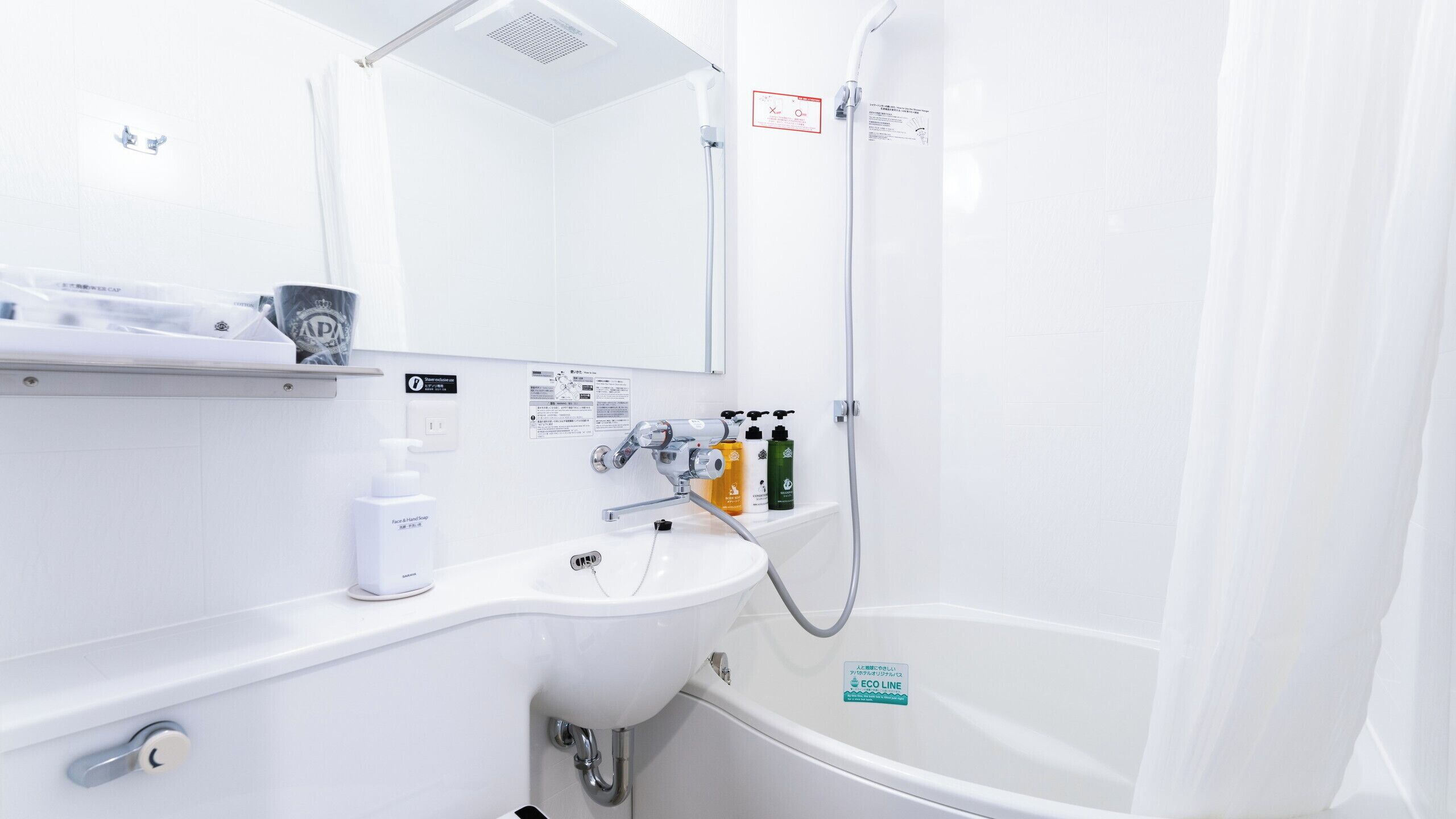 A modern bathroom with a white sink, a mirror, a shower, and a toilet. There are toiletries on the sink and a sign indicating an eco-friendly water system.