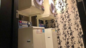 A laundry area with two washing machines, a control panel, and a wall with a floral pattern. - Apa Hotel A Namba Minami Ebisucho Ekia (Osaka)