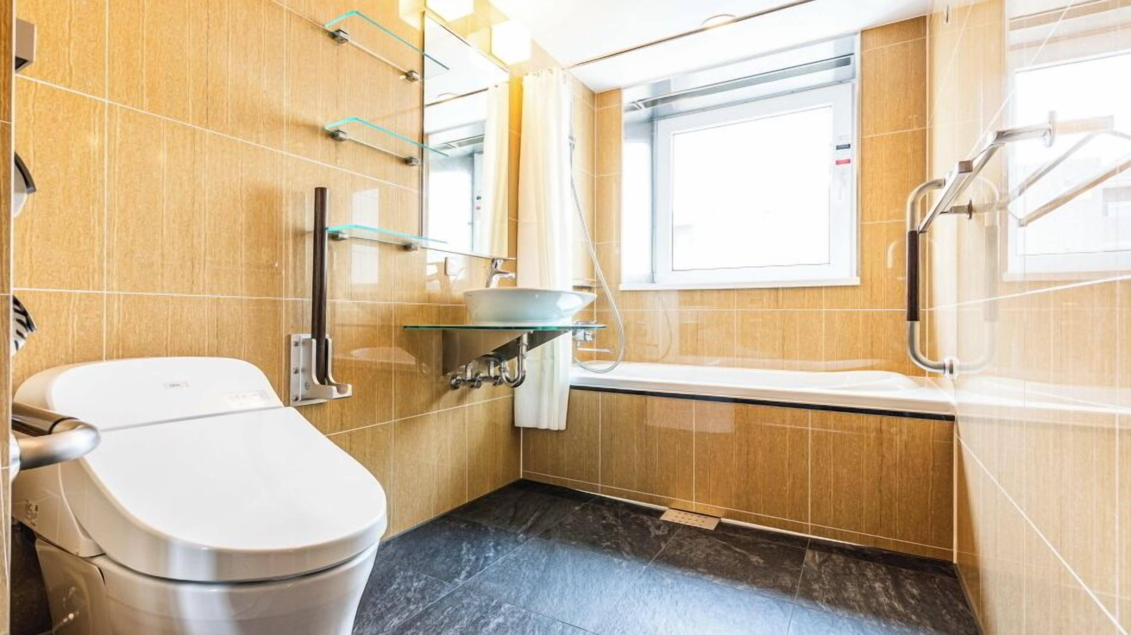 A compact bathroom with a toilet, a glass sink, a shower, and a window.