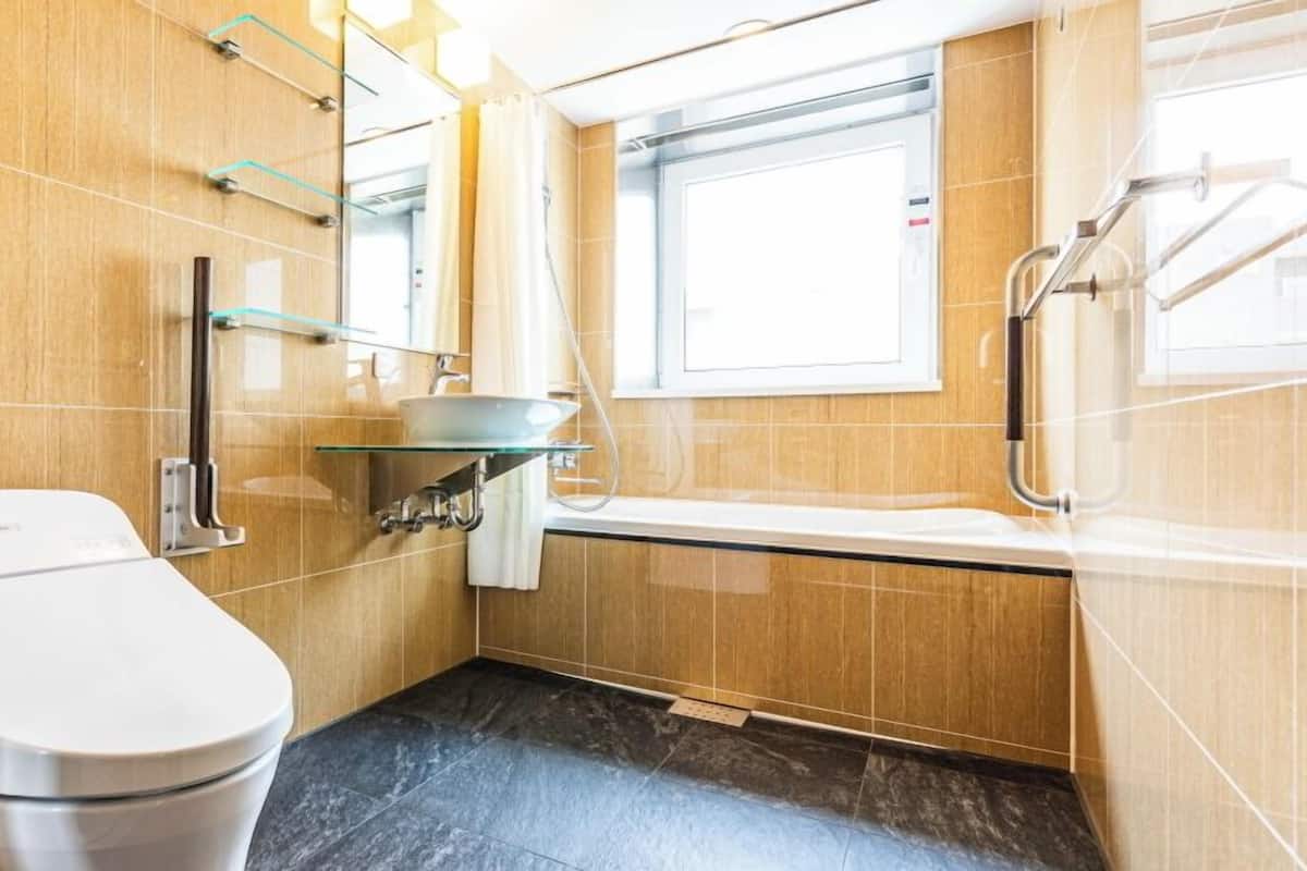 A compact bathroom with a toilet, a glass sink, a shower, and a window.