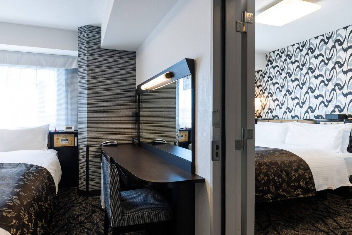 A hotel room with two beds, a desk, a chair, a mirror, a nightstand, and a patterned wall.