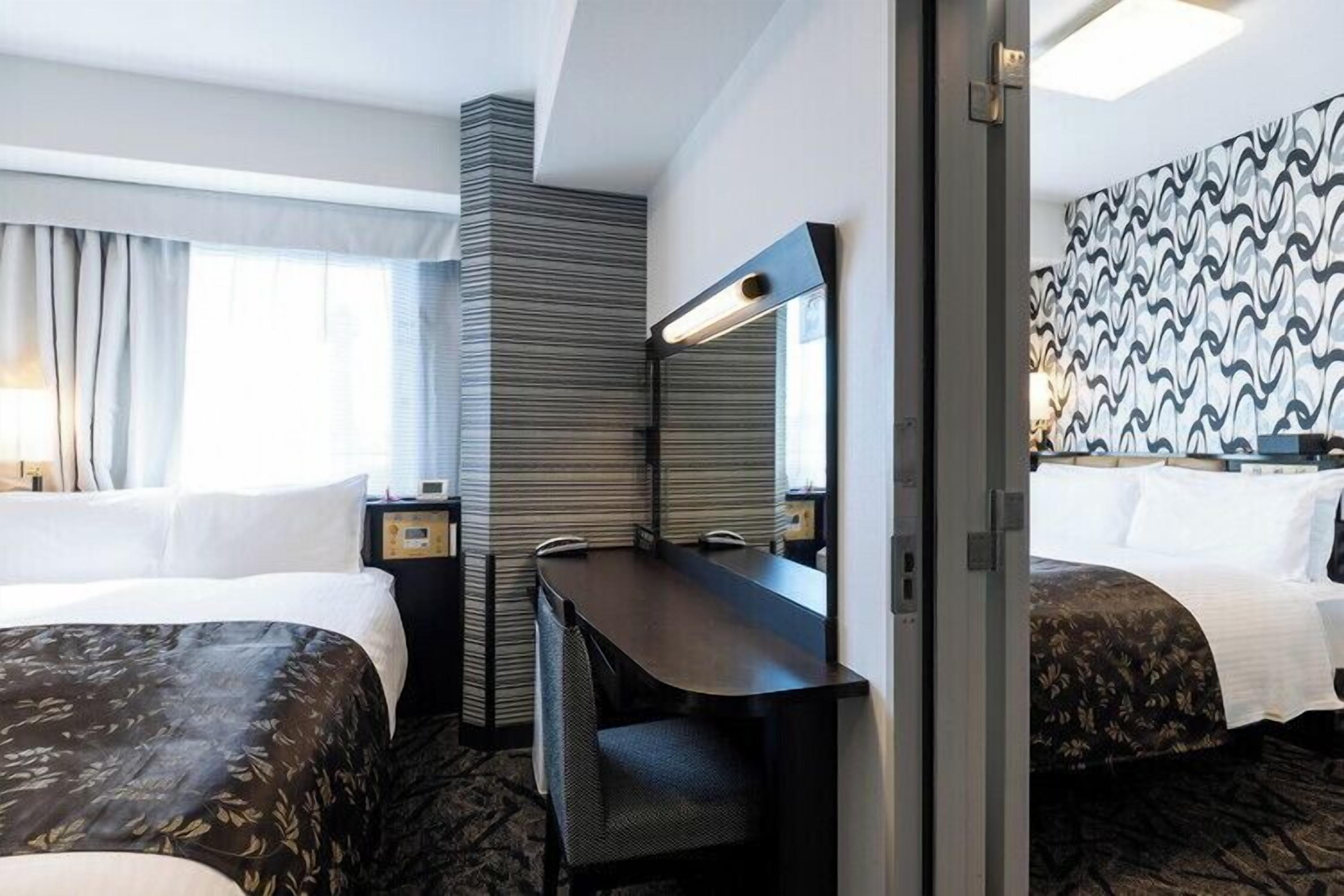 A hotel room with two beds, a desk, a mirror, and a patterned wall.
