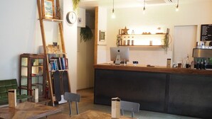 A cozy reception area with a wooden counter, a clock, a bookshelf, and a green sofa. - Almond Hostel And Cafe (Tokyo)