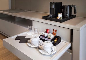 A breakfast tray with white cups, saucers, and a spoon, a coffee maker, and a box of assorted chocolates. - Hotel Kivir Sevilla (Seville)