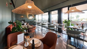 A restaurant with multiple tables, wicker lamps, and large windows. - Hotel Kivir Sevilla (Seville)
