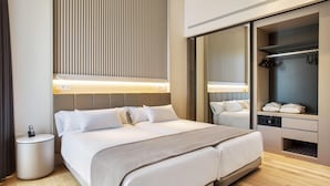 A modern hotel room with a large bed, a bedside table with a phone, a wardrobe with hanging clothes, and a mirror. - Hotel Kivir Sevilla (Seville)