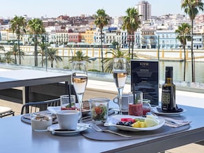 A table set with a glass of water, a cup, a plate of fruit, a bottle of olive oil, and a menu. - Hotel Kivir Sevilla (Seville)