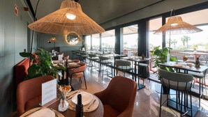 A restaurant with multiple tables, wicker lamps, and large windows. - Hotel Kivir Sevilla (Seville)